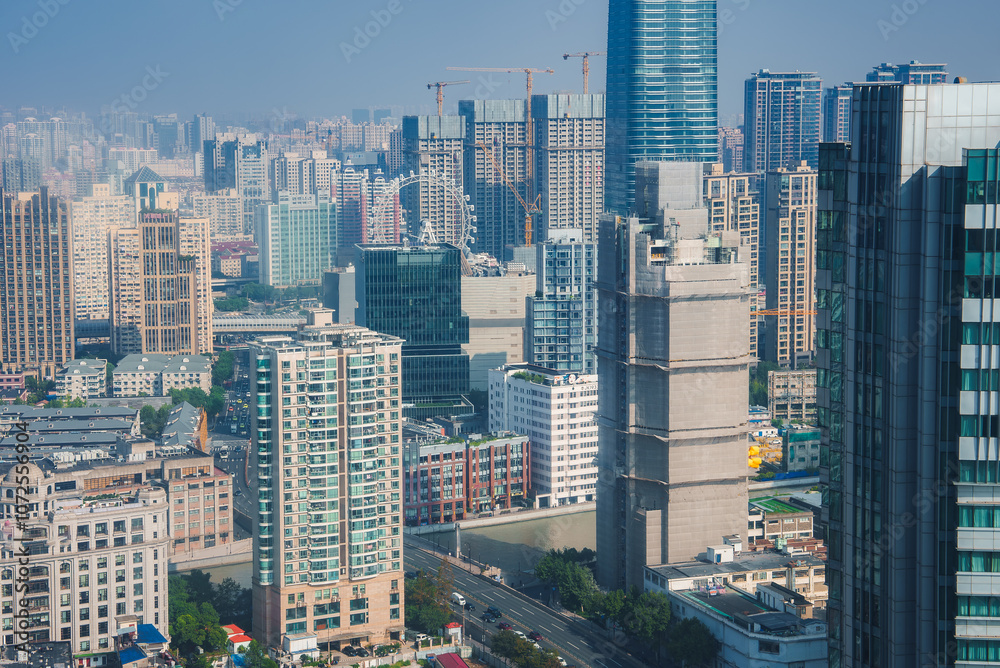 Fototapeta premium The image depicts Shanghai's dense skyline, featuring a tall cylindrical skyscraper, construction cranes, and a Ferris wheel in the background.