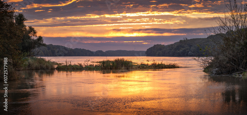 Sunrise idyll landscape on a river with a cloudy sky at golden hour