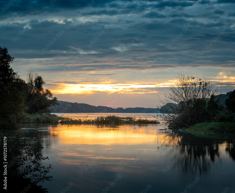 Obraz premium Sunrise idyll landscape on a river with a cloudy sky at golden hour