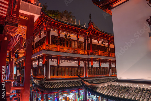 A traditional Chinese building in Shanghai's old town, featuring intricate wooden carvings, red accents, and upturned eaves, illuminated at night. photo