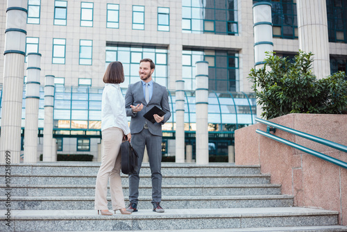 Successful young male and female businesspeople standing and talking on the stairs in front of an office building.