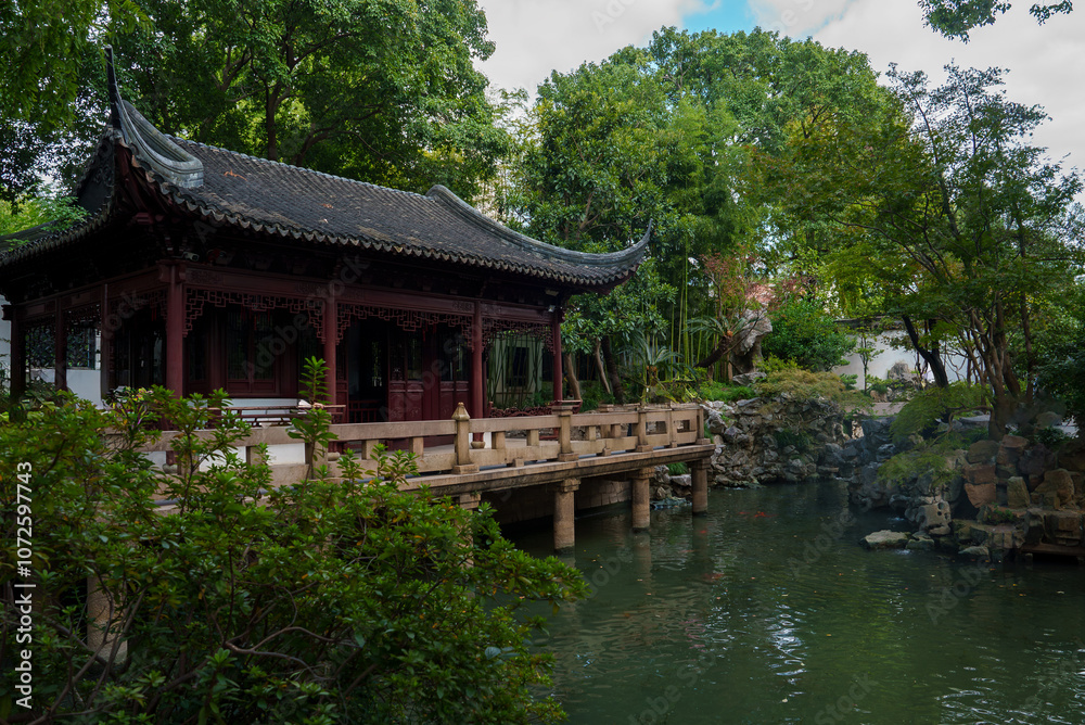 A traditional Chinese pavilion with curved eaves and wooden detailing stands by a pond. Lush greenery surrounds the scene, reflecting in the still water. A traditional Chinese pavilion with curved eaves and wooden detailing stands by a pond. Lush greenery surrounds the scene, reflecting in the still water.