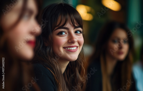 Close-up portrait of a smiling young woman in a relaxed social setting, surrounded by friends