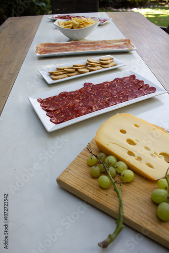 Green grapes and gruyere cheese on a wood board and pepperoni plate