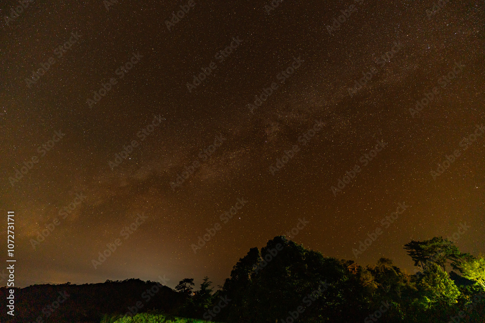 Fototapeta premium Time lapse Milky Way above mountains at night in autumn. Landscape with mountain valley, low clouds, purple starry sky with milky way. The Milky Way shines on a cold night in the north of Thailand