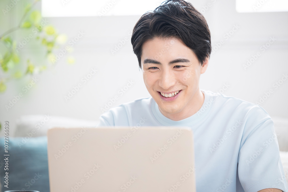 明るい部屋でパソコンを使う笑顔の若い男性 フリーランスやエンジニア、デザイナーなどの仕事をする人の爽やかなイメージのクローズアップ 明るい部屋でパソコンを使う笑顔の若い男性 フリーランスやエンジニア、デザイナーなどの仕事をする人の爽やかなイメージのクローズアップ