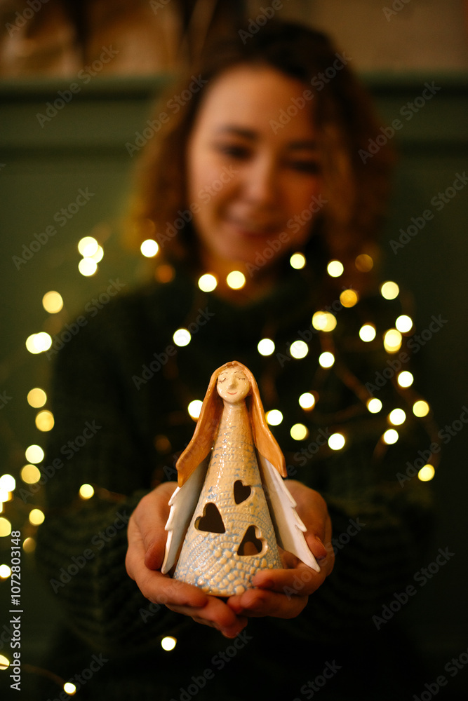 Fototapeta premium Festive Christmas image of woman hands holding angel figurine. Angel figurine in warm Christmas lights held by a woman hands, creating serene and festive mood, perfect for holiday , Angel Day content