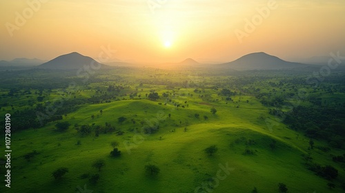 Serene tropical landscape at sunrise, with mist gently hovering over lush green fields and scattered trees, framed by distant mountains. photo