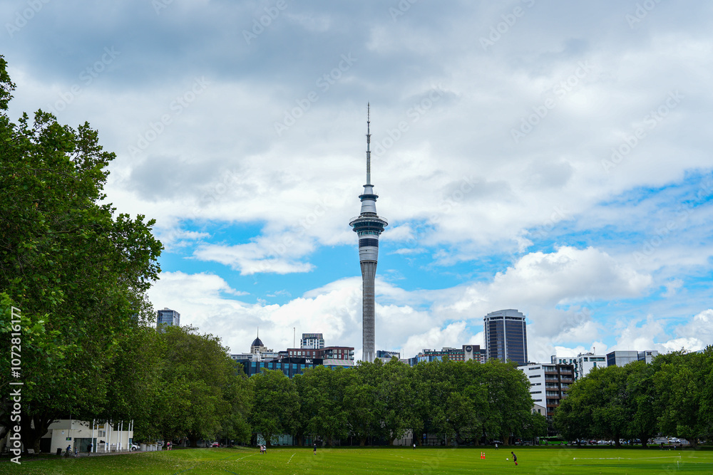 Naklejka premium A Scenic View of the Sky Tower Amidst Green Trees and Urban Landscape Under a Cloudy Sky in Auckland, New Zealand, Showcasing Beautiful Nature and Architecture