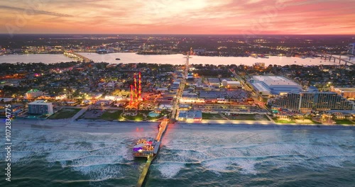 Tourist attractions on American southern seashore in Daytona Beach city, Florida at sunset. Illuminated Main Street Pier and Breakers Oceanfront Park. Luxurious hotels and apartment buildings.