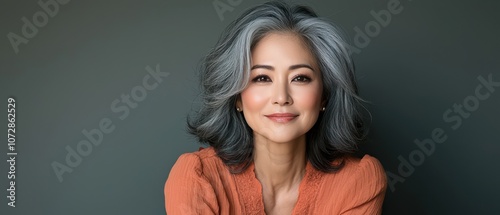 Confident woman with gray hair smiling warmly against a neutral background.