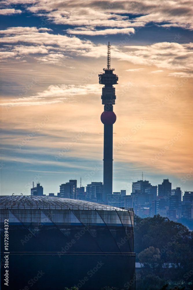 Fototapeta premium sunset over Hillbrow telecommunications Tower in city skyline in Johannesburg. surrounded by downtown buildings in Johannesburg, South Africa at down dusk late evening