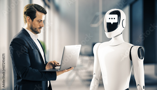 Fotografie Businessman looking at laptop while standing in front of a humanoid robot with a chat symbol on its face in office environment