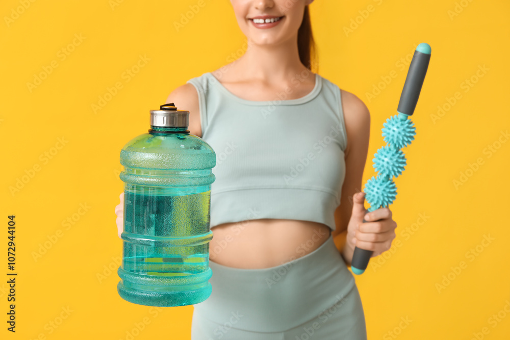 Beautiful young sporty happy woman with bottle of water and massager on yellow background, closeup Beautiful young sporty happy woman with bottle of water and massager on yellow background, closeup