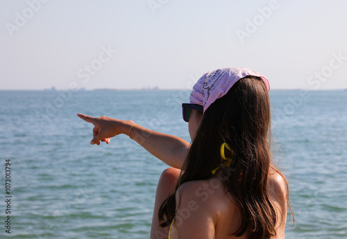 Valokuva girl with long brown hair wearing bandana pointing toward ocean on summer day