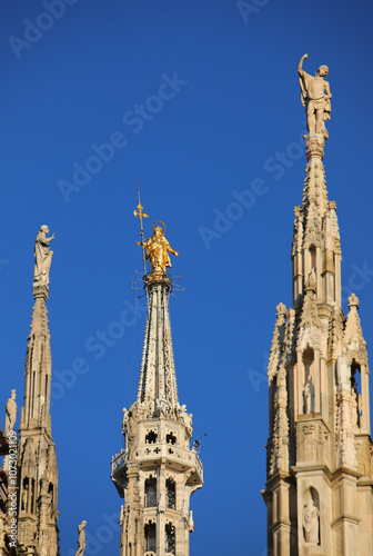 statue of Holy Virgin Madonna called Madonnina among tall Gothic spires at Milan Cathedral in Northern Italy