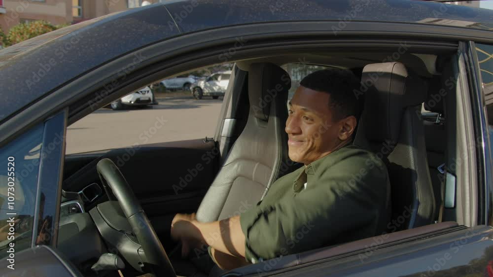Side view of positive carefree attractive black male driver sitting in vehicle, enjoying catching music, singing along and swaying to the beat while driving car in city street. Side view of positive carefree attractive black male driver sitting in vehicle, enjoying catching music, singing along and swaying to the beat while driving car in city street.
