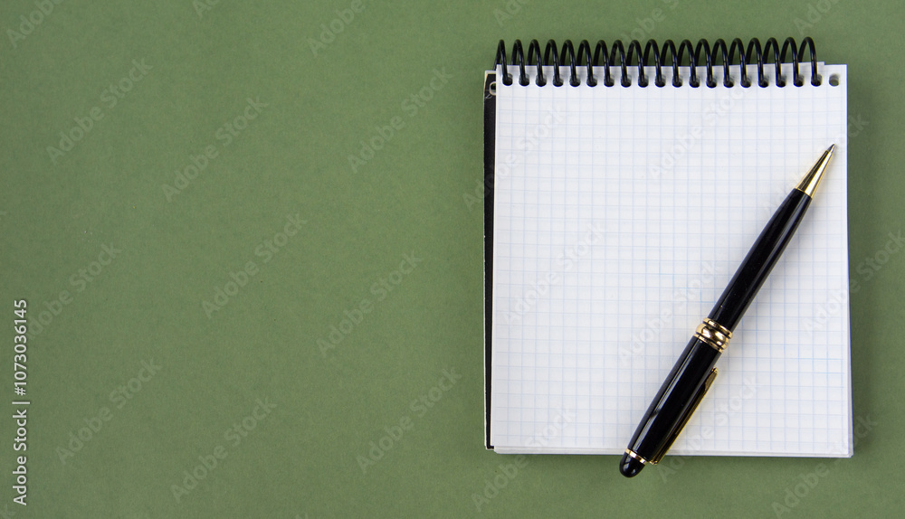 Top view of a notepad and pen on a green background. A place to record. The banner. Top view of a notepad and pen on a green background. A place to record. The banner.