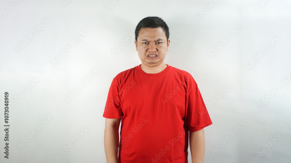 A young Indonesian man wearing a red t-shirt with a frown facing forward
