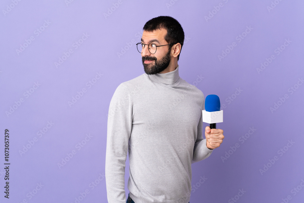 Adult reporter man with beard holding a microphone over isolated purple background . Portrait Adult reporter man with beard holding a microphone over isolated purple background . Portrait