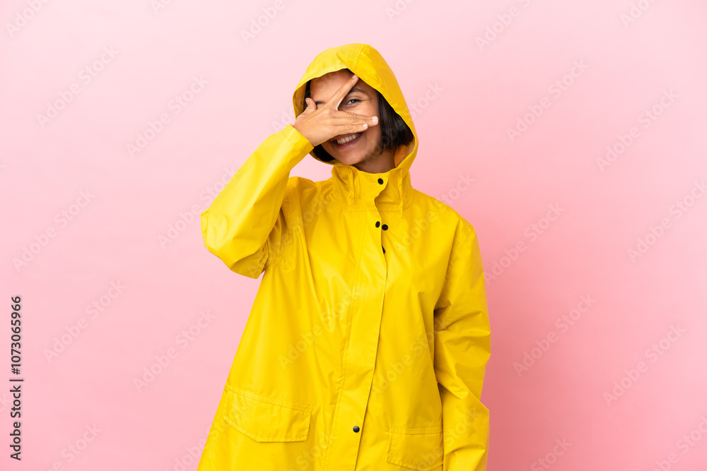 Young latin woman wearing a rainproof coat over isolated background covering eyes by hands and smiling Young latin woman wearing a rainproof coat over isolated background covering eyes by hands and smiling