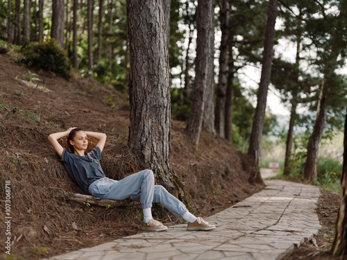 Young woman relaxing on a forest path, enjoying nature with a serene expression, dressed casually in a comfortable t shirt and jeans Nature and relaxation concept