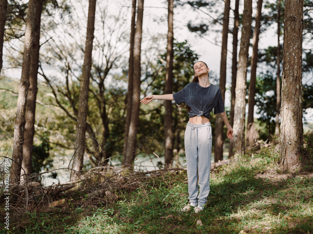 Free spirited young woman enjoying nature in a forest, arms outstretched, wearing casual grey outfit with loose top and sweatpants Serenity and freedom concept Free spirited young woman enjoying nature in a forest, arms outstretched, wearing casual grey outfit with loose top and sweatpants Serenity and freedom concept