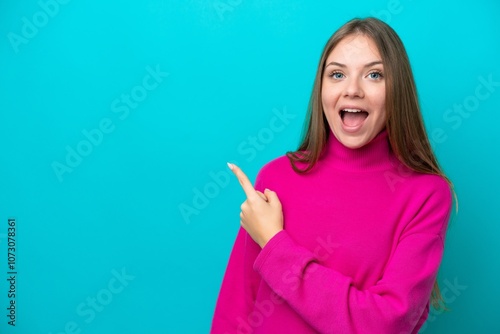 Young Lithuanian woman isolated on blue background surprised and pointing side