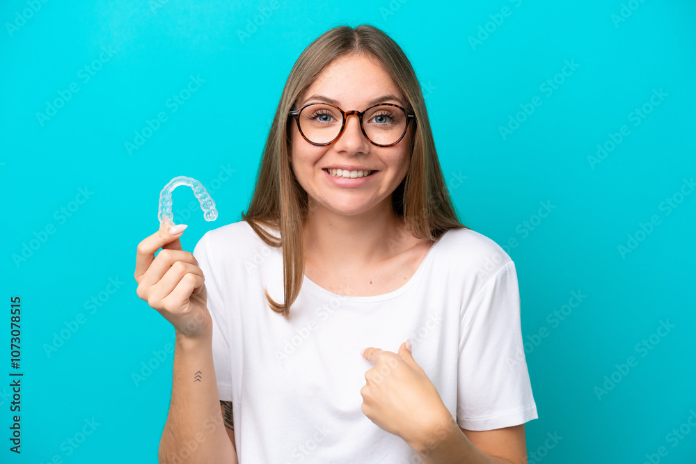 Young Lithuanian woman holding invisible braces isolated on blue background with surprise facial expression