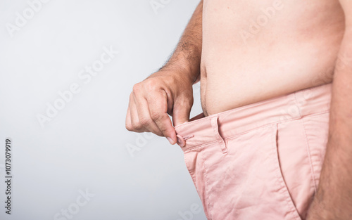 Foto Man with a larger physique stands adjusting the waistband of his pants to check