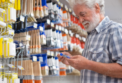 Senior man makes purchases in a hardware store chooses tools for repair or improvement home