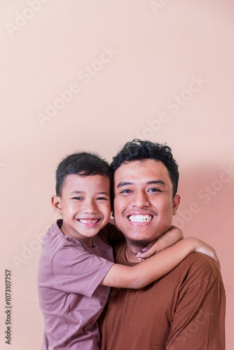 an asian boy hugs his father facing the camera with a happy expression