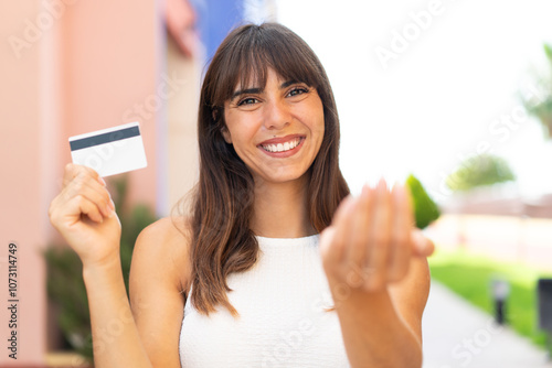 Young woman holding a credit card at outdoors inviting to come with hand. Happy that you came