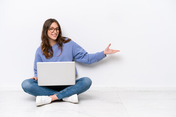 Young caucasian woman with a laptop sitting on the floor isolated on white background extending hands to the side for inviting to come