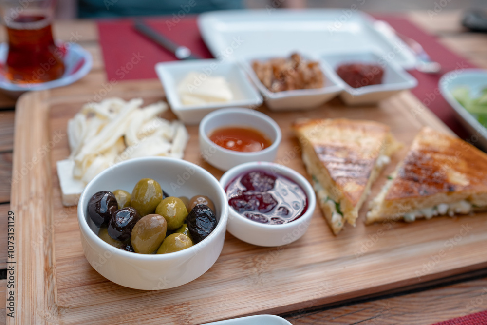 Traditional Turkish breakfast spread with fresh bread, olives, cheese, tomatoes, cucumbers, and variety of jams and spreads. Enjoyed in vibrant setting, capturing essence of Turkish morning culture.
