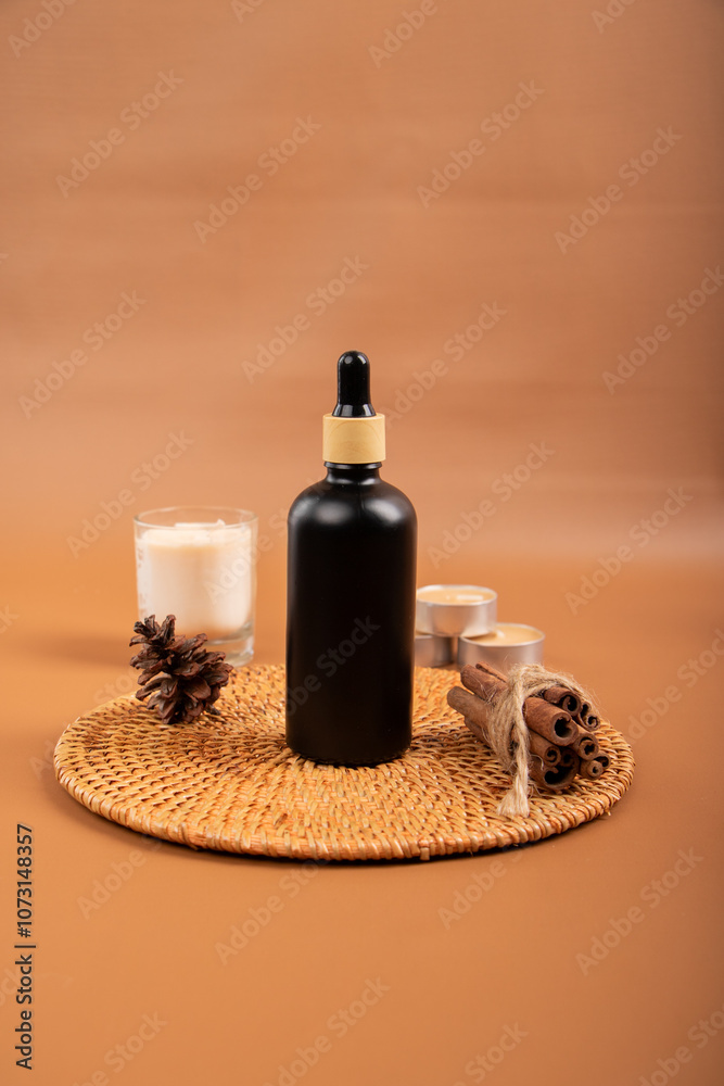 Black Dropper Bottle with Candle and Cinnamon on Woven Mat for Spa and Skincare