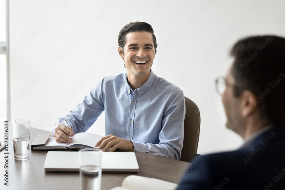 Happy young Latin business leader man meeting with partner at table, discussing cooperation terms, creative ideas for startup project, smiling, laughing, enjoying teamwork, collaboration Happy young Latin business leader man meeting with partner at table, discussing cooperation terms, creative ideas for startup project, smiling, laughing, enjoying teamwork, collaboration