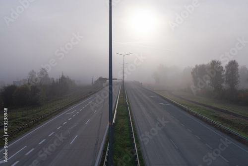 Obraz na płótnie Dwujezdniowa, czteropasmowa autostrada. Nad jezdnią unosi się mgła ograniczająca widoczność. Jest ona od przodu oświetlana promieniami słońca. w salonie