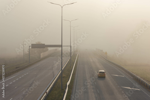 Obraz na płótnie Dwujezdniowa, czteropasmowa autostrada. Nad jezdnią unosi się mgła ograniczająca widoczność. Jest ona od przodu oświetlana promieniami słońca. w salonie