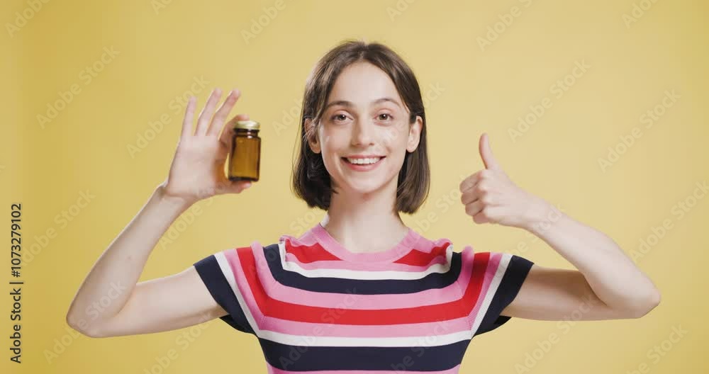 Young woman showcasing an empty brown pill bottle on a yellow background, displaying contentment Young woman showcasing an empty brown pill bottle on a yellow background, displaying contentment