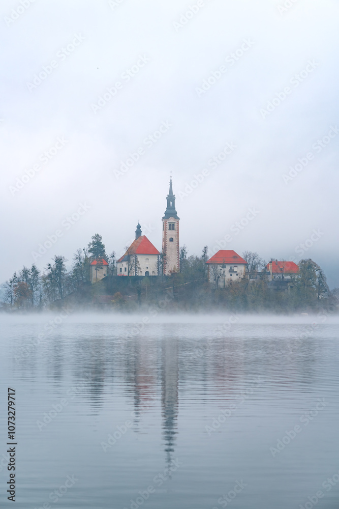 Late autumn on Lake Bled. Morning misty landscape. Travel in Slovenia. Picturesque church on the island on Lake Bled in autumn morning Late autumn on Lake Bled. Morning misty landscape. Travel in Slovenia. Picturesque church on the island on Lake Bled in autumn morning