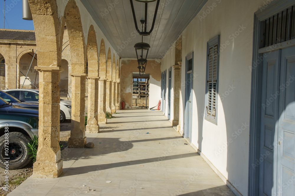 Obraz premium A sunlit corridor framed by classic arches in an old stone building during a serene afternoon.