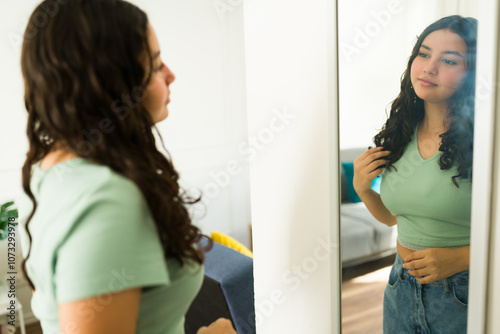 Latin teenage girl at home admiring herself in the mirror, gently caressing her hair and smiling