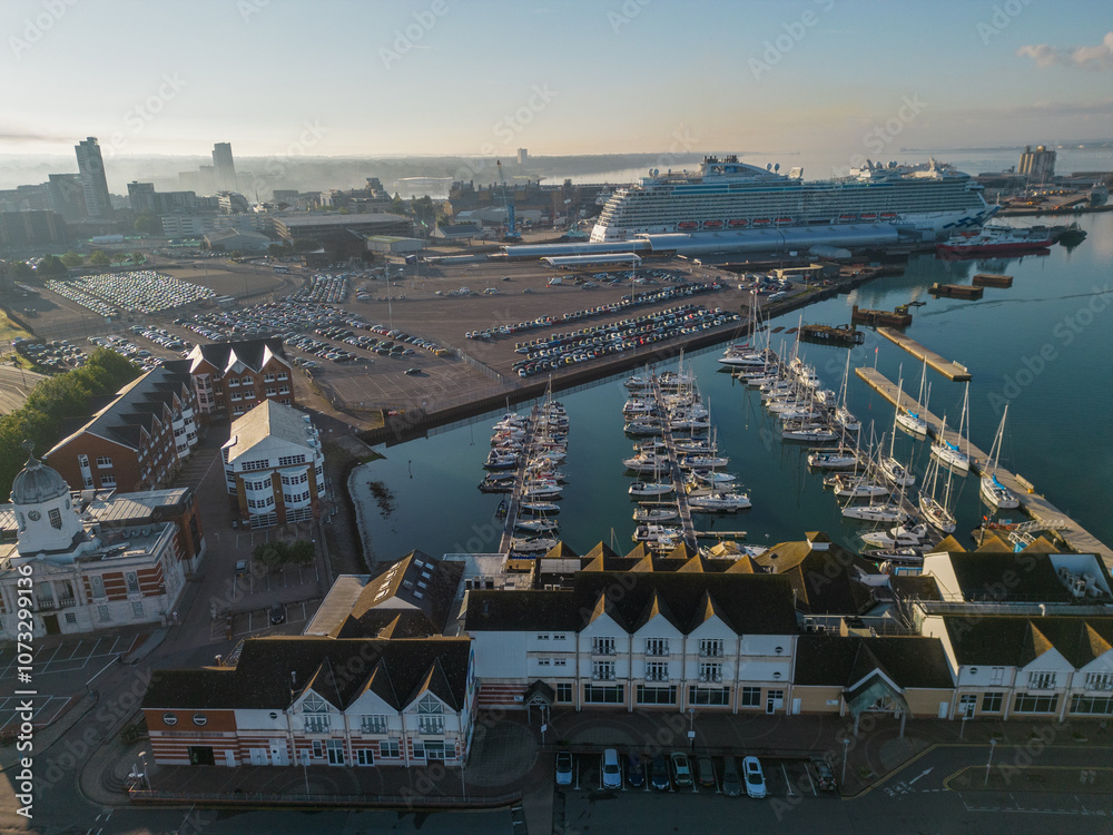 Southampton UK Town Quay Marina and passenger terminal with large cruise ship. Aerial view on a sunny morning. Hazy sky from smoke air pollution. Mirror like calm blue sea with sailing boats mooring.