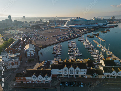 Obraz na płótnie Southampton UK Town Quay Marina and passenger terminal with large cruise ship. Aerial view on a sunny morning. Hazy sky from smoke air pollution. Mirror like calm blue sea with sailing boats mooring. w salonie