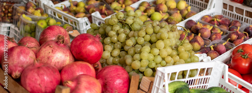 Pomegranate, grapes, figs and other fresh ripe fruits in boxes close-up at market