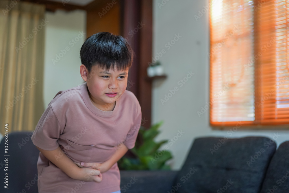 Portrait of sick unhappy little child asian boy touching belly stomach with suffering from stomach ache pain, gastritis, gastroenteritis, food poisoning, diarrhea, intestinal inflammation at home Portrait of sick unhappy little child asian boy touching belly stomach with suffering from stomach ache pain, gastritis, gastroenteritis, food poisoning, diarrhea, intestinal inflammation at home