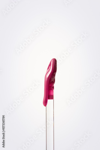 Vertical close-up shot of a purple lip gloss that flows down the wand on a clean white background. Minimal pink makeup aesthetics.