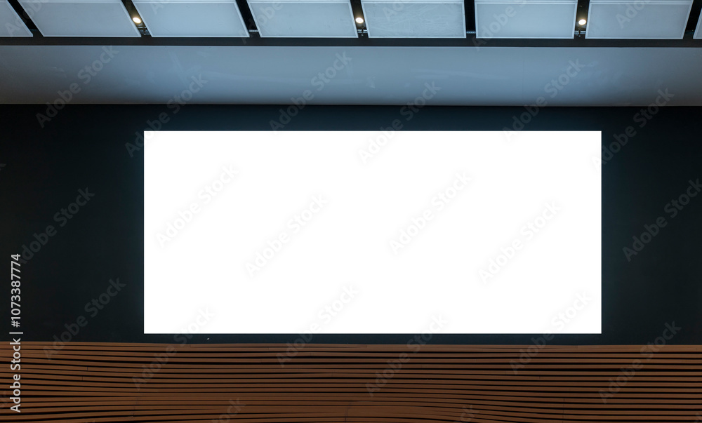 Blank white screen mounted on black wall in modern interior space with wood panel accents at bottom. Ceiling lights and white ceiling panels add minimalist feel to setting Blank white screen mounted on black wall in modern interior space with wood panel accents at bottom. Ceiling lights and white ceiling panels add minimalist feel to setting
