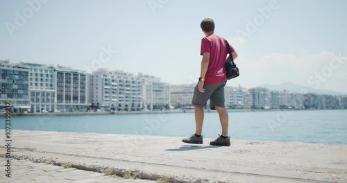 Young man enjoying a sunny day by the sea at a quayside with city background